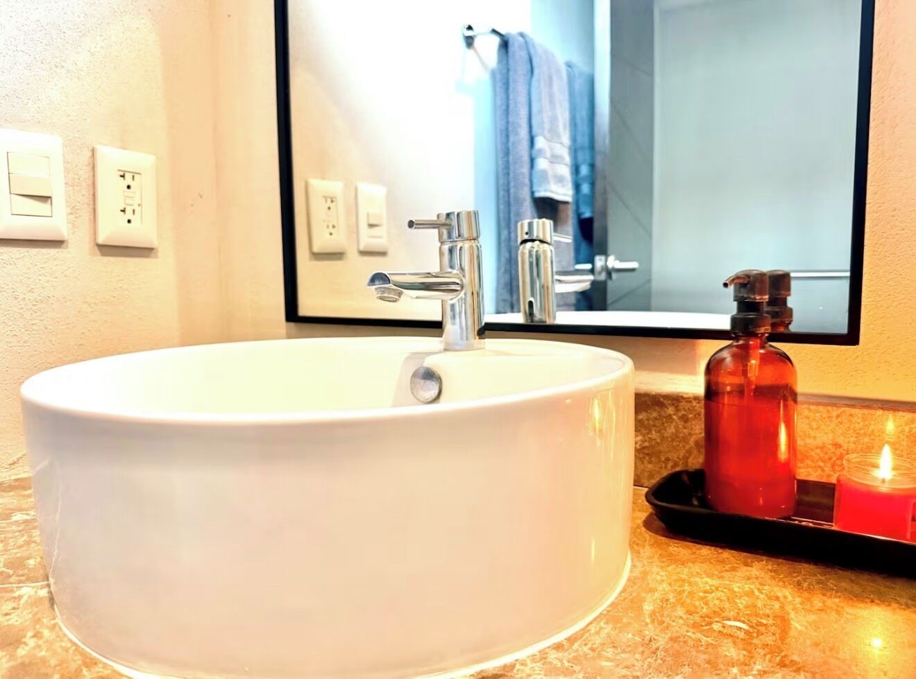 A white bathroom sink with a modern faucet, a mirror above it, and a candle on the countertop.