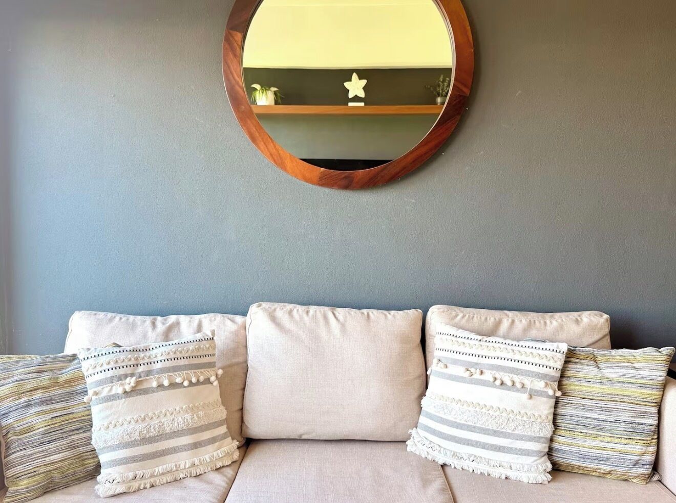 A sofa with three pillows, a round mirror, and a star decoration on the wall.