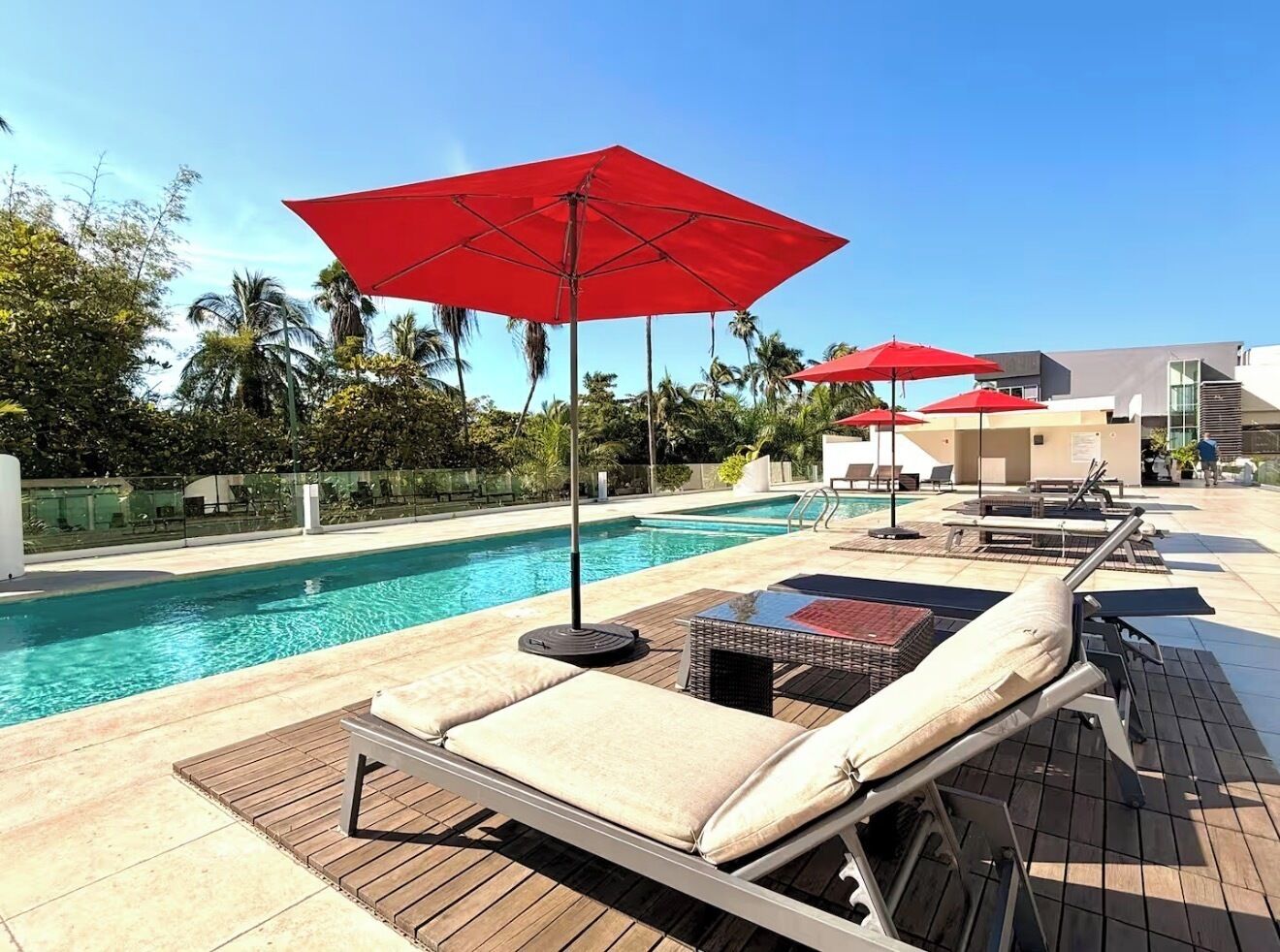 A poolside area with lounge chairs, red umbrellas, and a clear view of the pool.