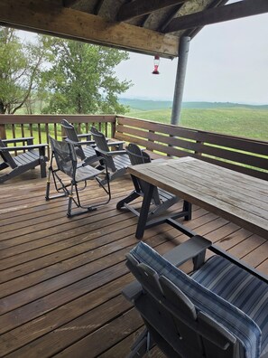 A wooden deck with outdoor seating, including chairs and a table, overlooking a grassy landscape.