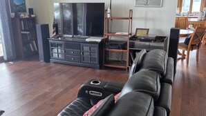 Una sala de estar con un sofá de cuero, un televisor, un mueble de entretenimiento de madera y un comedor con una mesa y sillas.