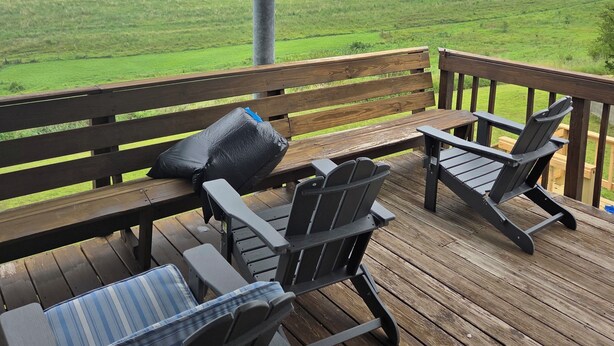 Un área de estar al aire libre cubierta con un banco y dos sillas Adirondack, con vista a un campo verde.