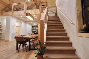 A wooden staircase leading to an upper level, a dining area with a wooden table and chairs, and a potted plant.