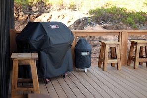 Una parrilla cubierta y una bolsa Weber sobre una terraza de madera, con taburetes.