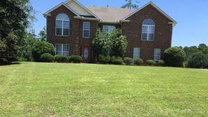 A two-story brick house with a well-maintained lawn, a red door, and a small garden with bushes. - Spacious 4-bedroom house in tranquil Jonesboro with AC (Jonesboro)