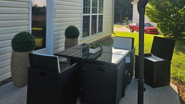 An outdoor patio with wicker furniture, a glass-top table, and a black umbrella. - Spacious 4-bedroom house in tranquil Jonesboro with AC (Jonesboro)