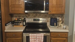 A kitchen with wooden cabinets, a stainless steel microwave, a stove, and a coffee maker. - Spacious 4-bedroom house in tranquil Jonesboro with AC (Jonesboro)