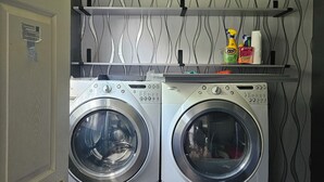 A laundry room with two front-loading washing machines, a shelf with cleaning supplies, and a patterned wall. - Spacious 4-bedroom house in tranquil Jonesboro with AC (Jonesboro)