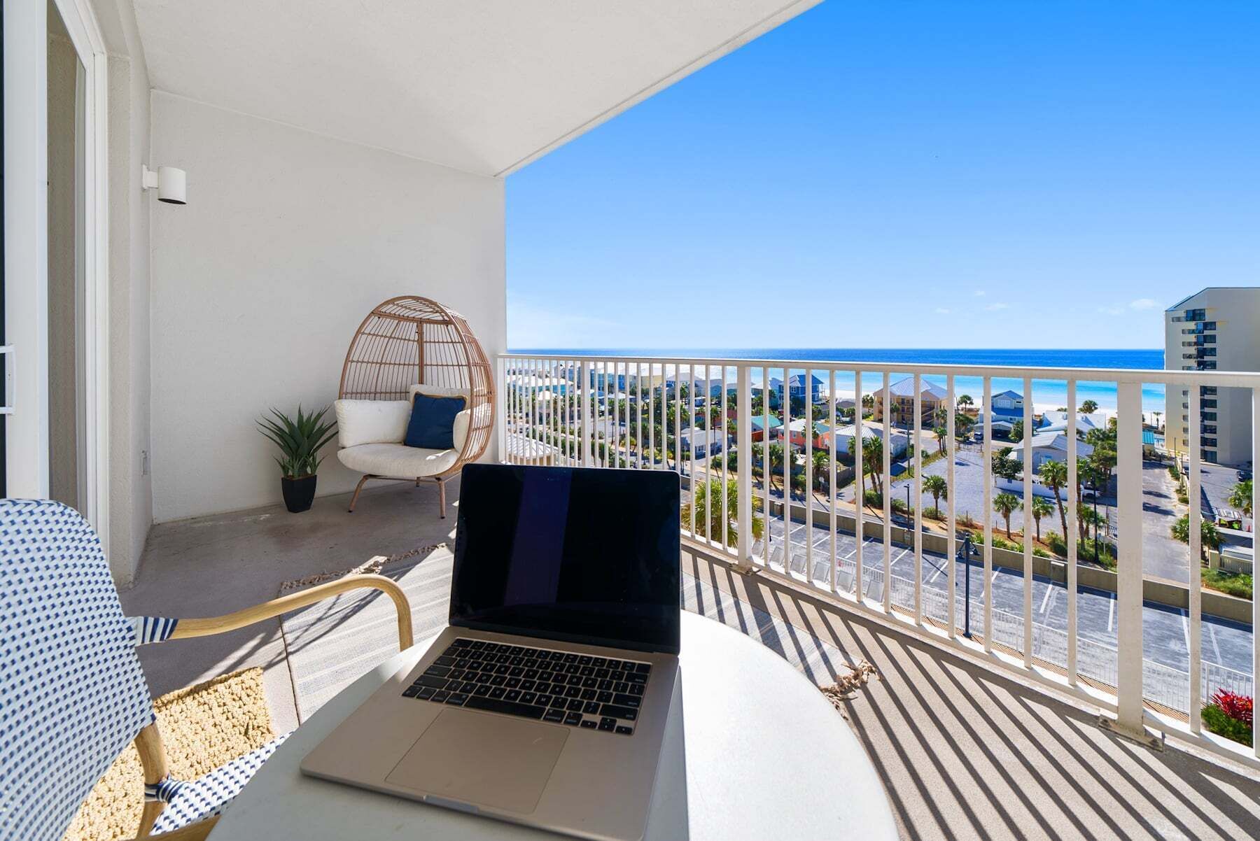 A balcony with a laptop, a wicker chair, and a view of the city and ocean.