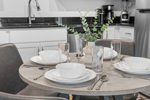 A round dining table with white plates, bowls, and cutlery, a vase with green foliage, and a modern kitchen in the background. - Relaxing Lake Taneycomo Condo Steps from Downtown Branson (Branson)