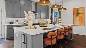 A modern kitchen with grey cabinets, a white island, and orange bar stools. - Delightful 4 Bedroom Home with Hot Tub, Game Rm, Putt Putt,Near Mercedez Stadium (Atlanta)