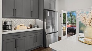 A modern kitchen with grey cabinets, a stainless steel refrigerator, a coffee maker, and a toaster. - Delightful 4 Bedroom Home with Hot Tub, Game Rm, Putt Putt,Near Mercedez Stadium (Atlanta)
