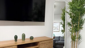 Moderni olohuone, jossa on suuri litteänäyttöinen televisio, puinen mediakeskus, peili ja ruukussa oleva bambukasvi.