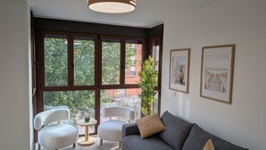 Olohuoneessa on sohva, kaksi nojatuolia, pieni pöytä, viherkasvi ja seinällä on kehystettyjä valokuvia.