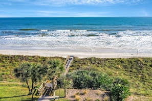 A beach with a wooden walkway leading to the shore, surrounded by greenery and palm trees. - Oceanfront Luxury Condo | Renovated | Private Beach Access | Pools | Tennis Court (St. Augustine)