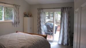 Un dormitorio con cama, armario, ventilador de techo y puerta corrediza de vidrio que da a un área exterior con sillas y una barbacoa.