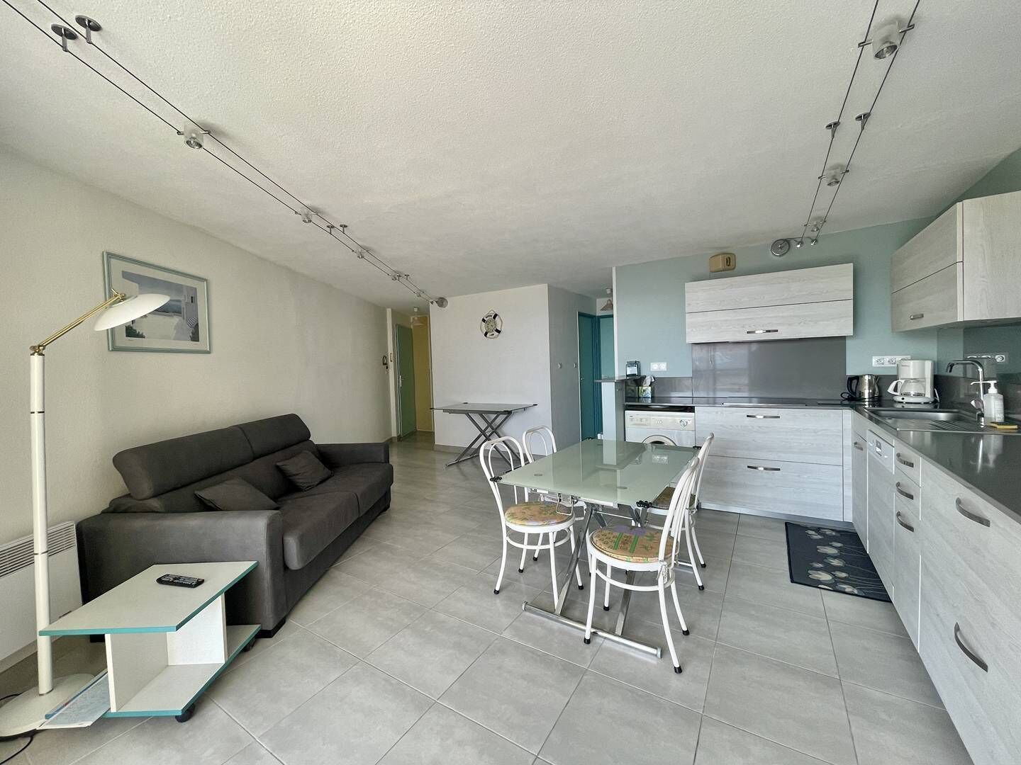 Un appartement moderne comprenant un coin repas, une kitchenette et un canapé gris.