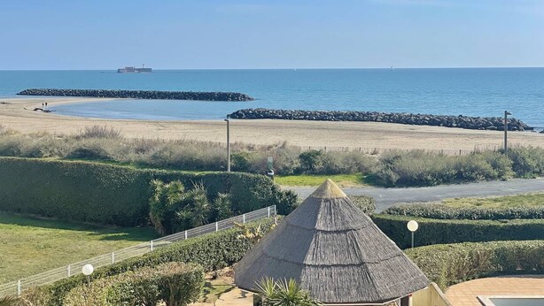 A beach view with a thatched-roof structure, a paved walkway, and a distant ship. - CAP D'AGDE - Rochelongue / Réf 417 (CAP D'AGDE)
