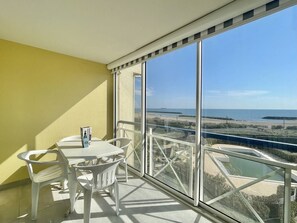 Ein Balkon mit Tisch und Stühlen und Blick auf das Meer, unter einem wolkenlosen Himmel.