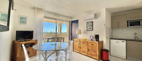 Una cocina moderna con microondas, pileta y lavavajillas, un comedor con mesa y sillas de vidrio, y vistas a través de un ventanal.
