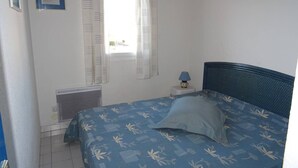 Ein Schlafzimmer mit Bett, Fenster mit Vorhängen, Nachttisch mit Lampe und Heizkörper.