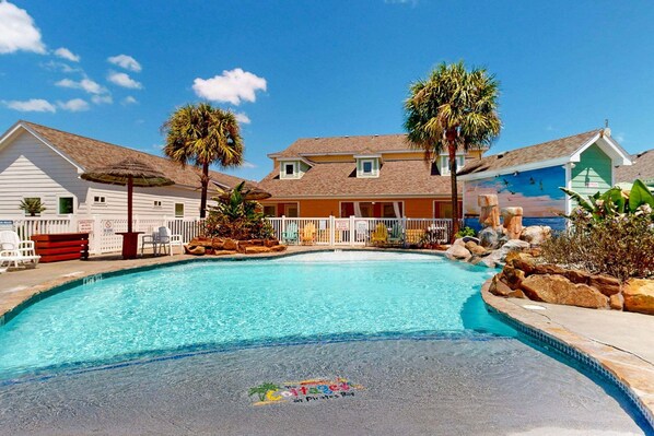 A swimming pool with a tropical theme, surrounded by buildings with a beachside view. - PB117 Shared Pool, Pet Friendly, Parking for 3, Charcoal Grill (Port Aransas)