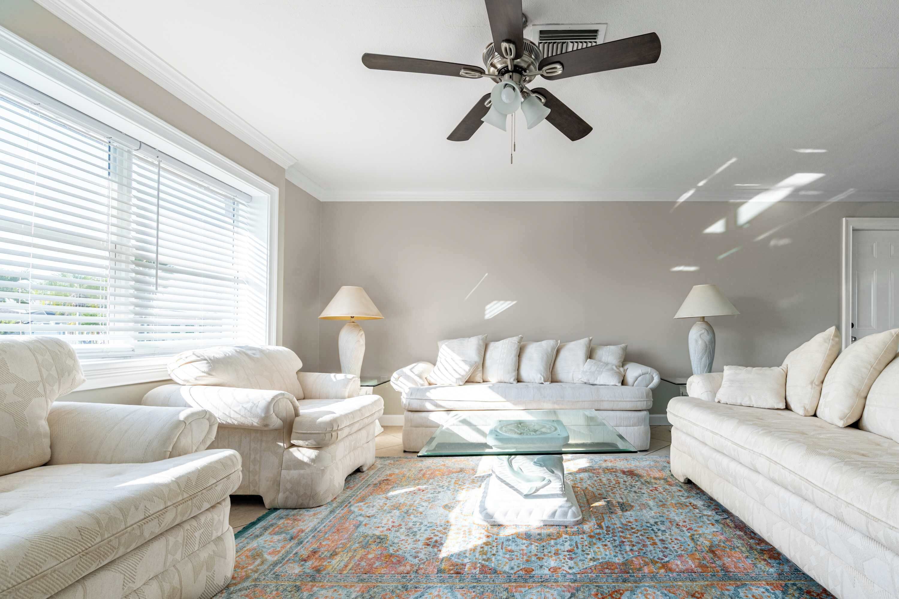Un salon doté d’un ventilateur de plafond, de meubles blancs et d’un tapis à motifs.