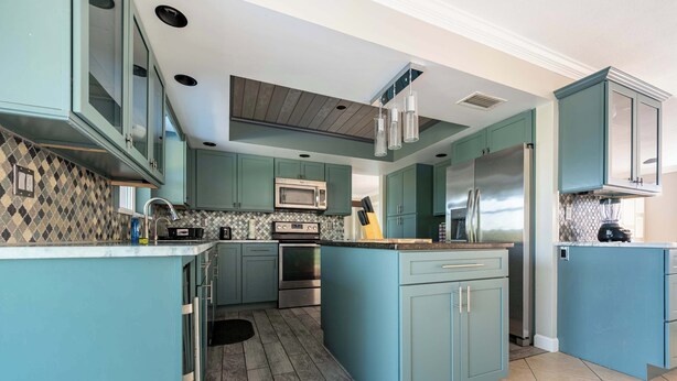 Una cucina con mobili color petrolio, un'isola centrale, elettrodomestici in acciaio inossidabile e un pannello di rivestimento decorato.