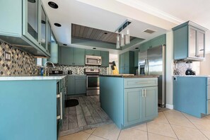 A kitchen with teal cabinetry, a central island, stainless steel appliances, and a patterned backsplash. - Private 3BR Pool House in Quiet Golf Community (Rotonda West)
