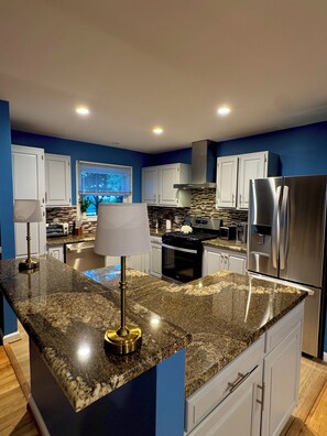 A modern kitchen with granite countertops, stainless steel appliances, and blue walls. - Rockville Private Oasis (Rockville)