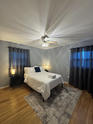 Ein Schlafzimmer mit einem Bett, einem Deckenventilator, einem Nachttisch mit Lampe und einem Teppich.