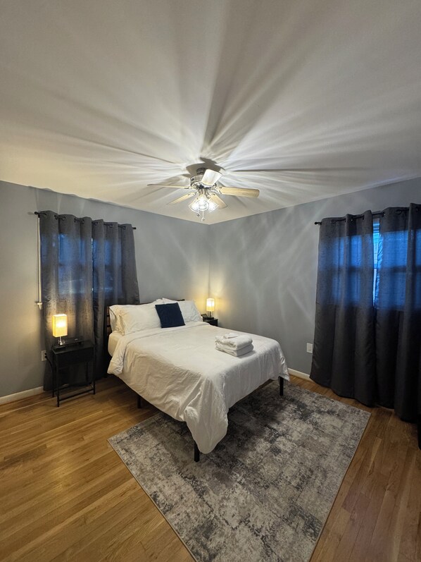 A bedroom with a bed, a ceiling fan, a nightstand with a lamp, and a rug.