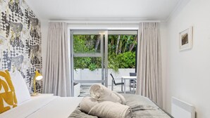 Ett hotellrum med en säng, en lampa, ett fönster med gardiner och utsikt över grönområden utanför.
