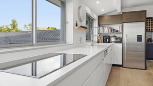 Ett modernt kök med en stor köksö, inbyggda vitvaror och utsikt över omgivningen.