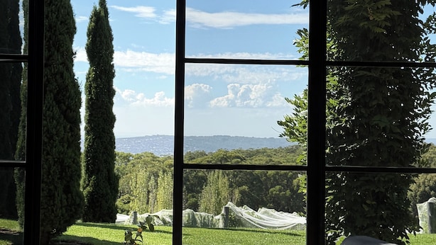 Ein modernes Interieur mit großen Fenstern, das einen Blick auf einen angelegten Garten und die entfernten Hügel bietet.