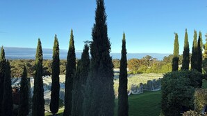 Ein angelegter Garten mit hohen Zypressen, einer grünen Rasenfläche und Blick auf das Meer.