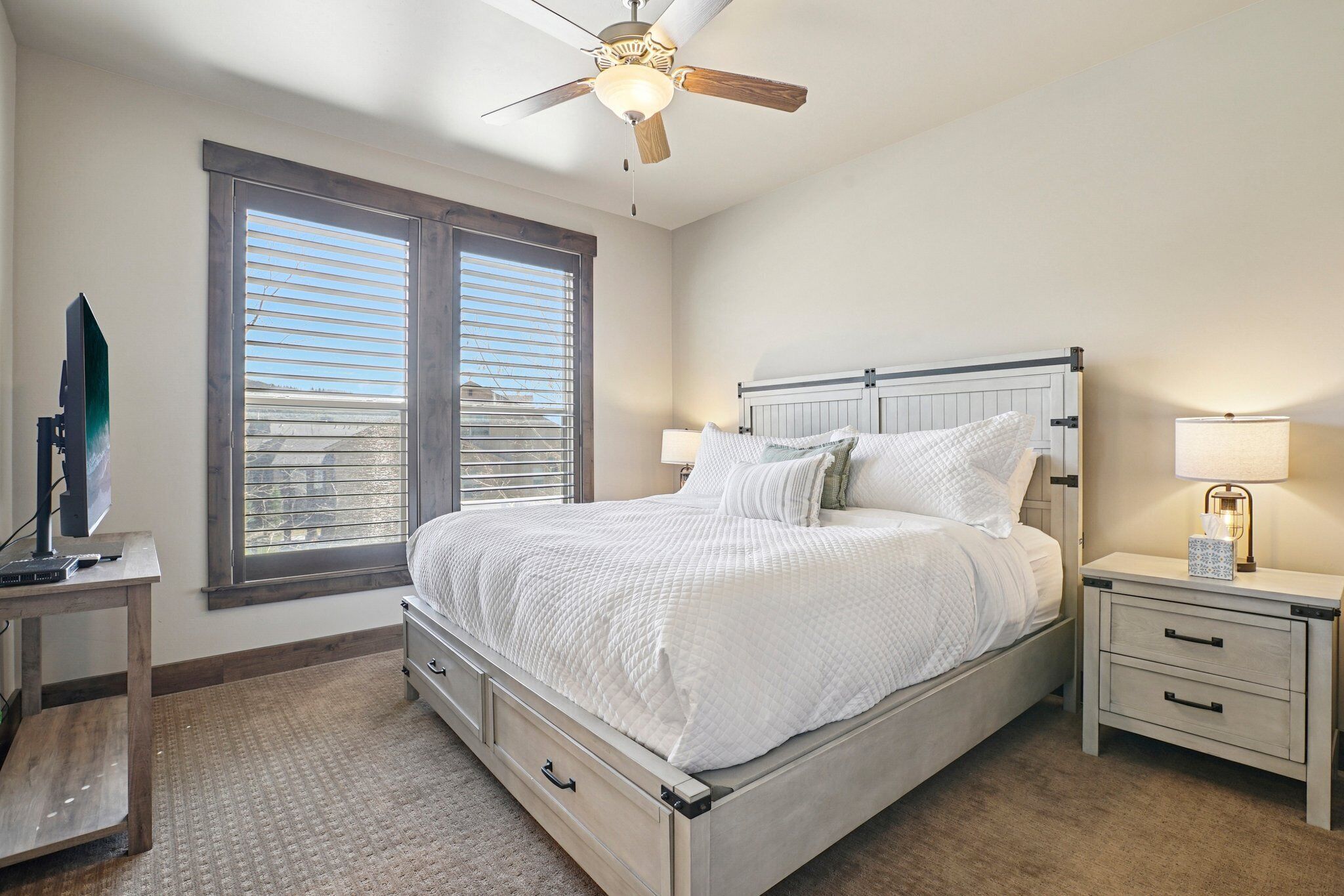 A bedroom with a bed, bedside tables, a ceiling fan, and a window with blinds.