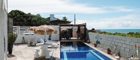 Un área de piscina con sillones de descanso, una mesa y sombrillas.