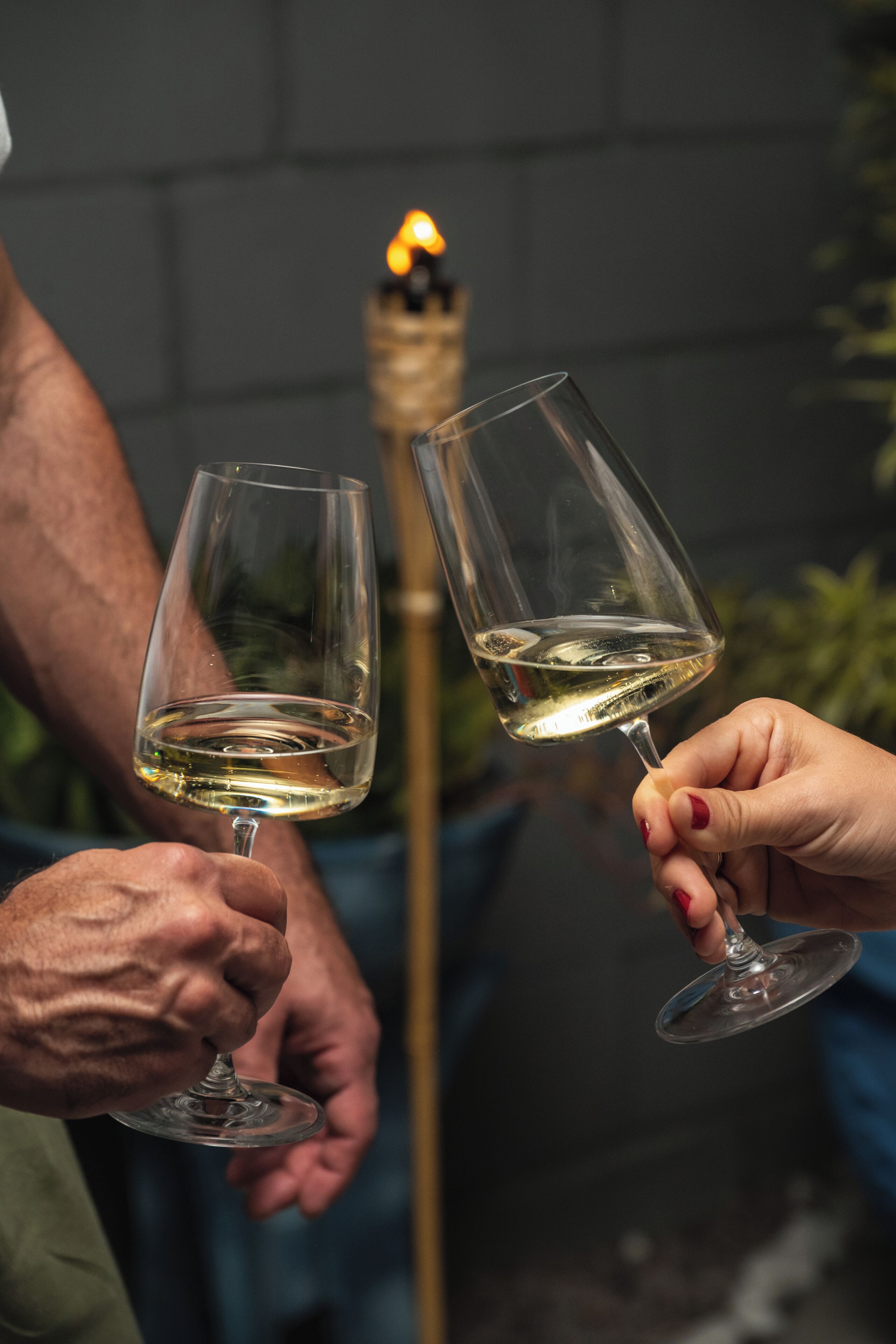 Dos personas sosteniendo copas de vino con una vela encendida al fondo.