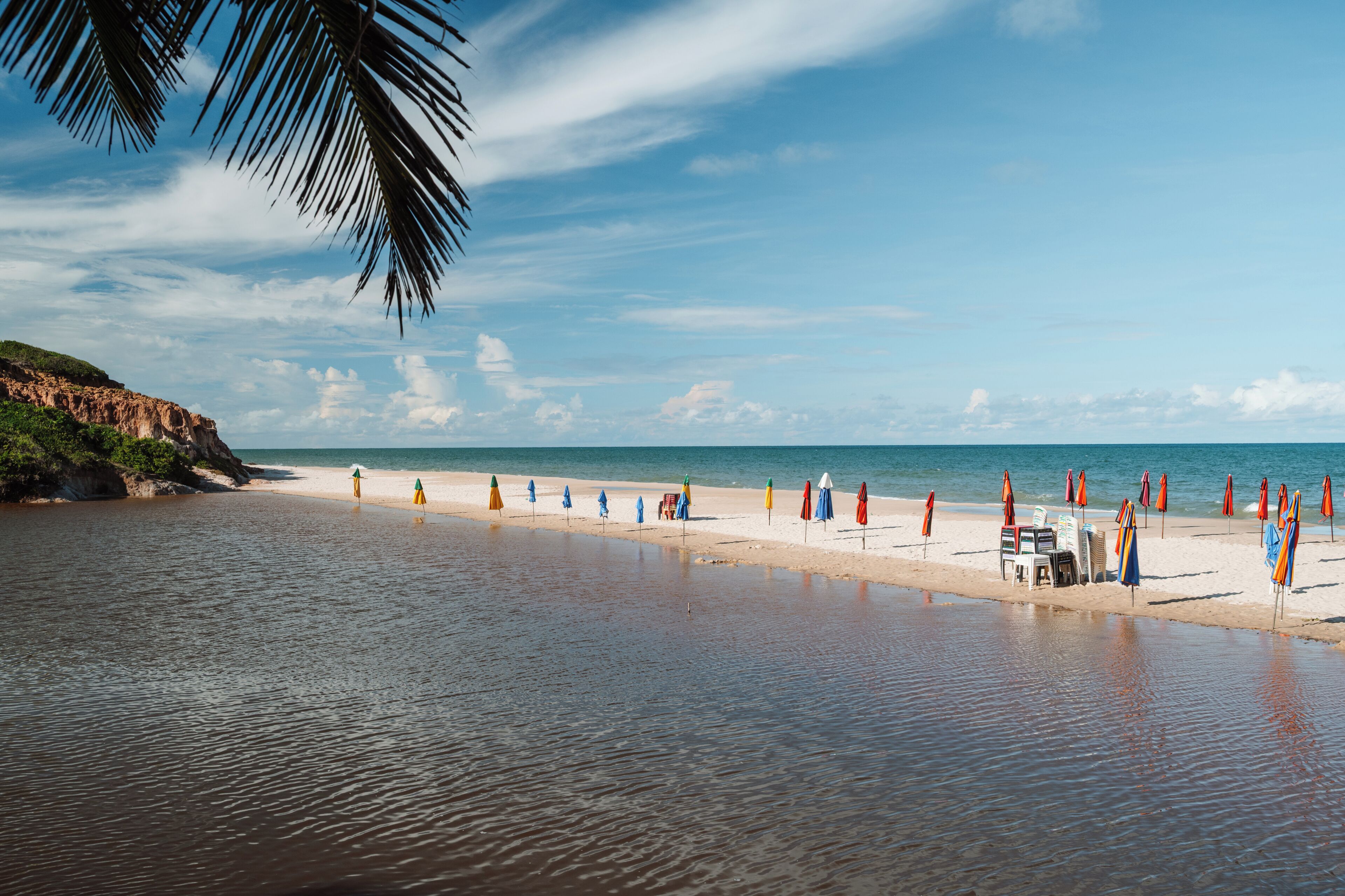 Ein Strand mit Sonnenschirmen und Liegestühlen, ruhigem Meer und blauem Himmel.