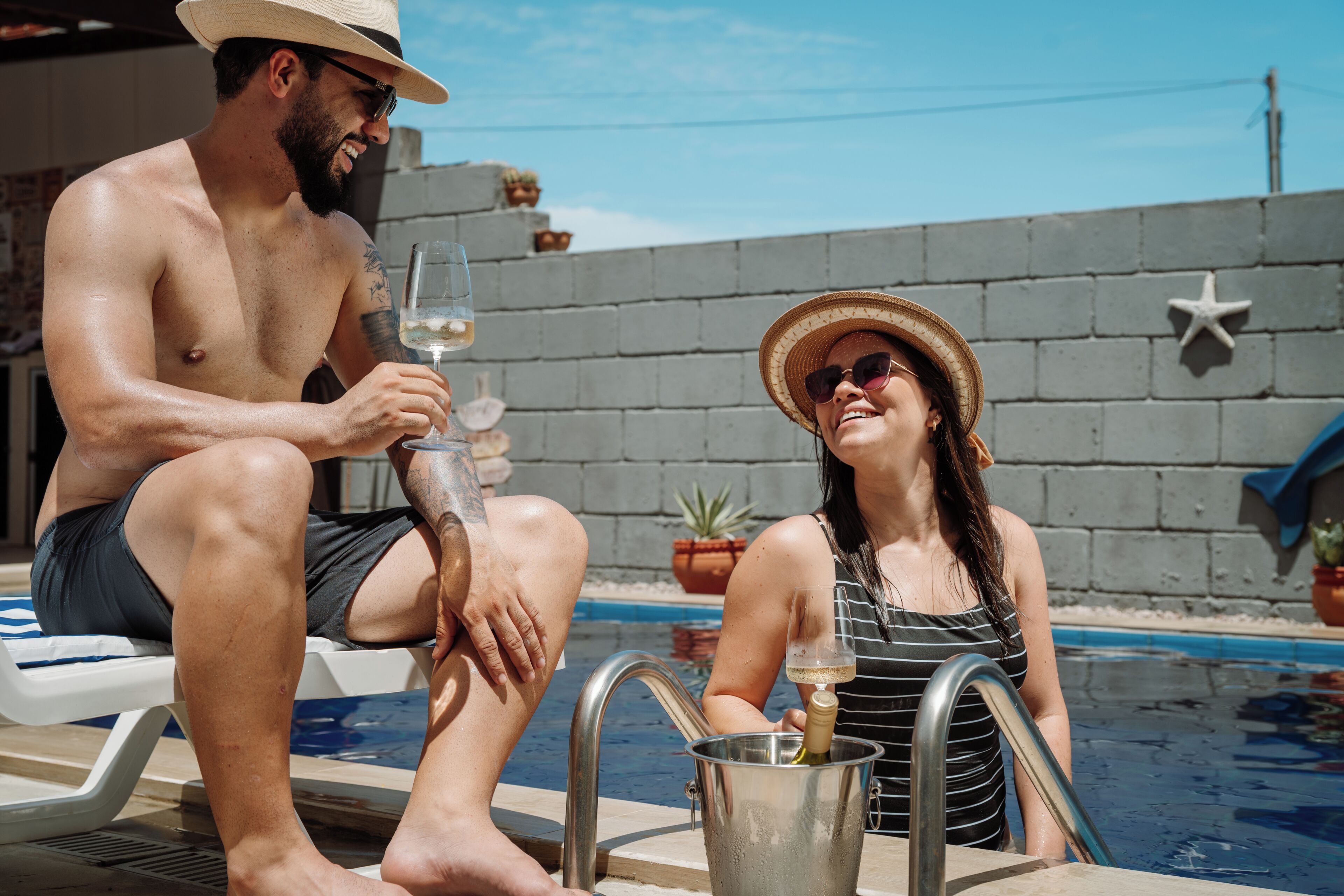 Un hombre y una mujer sentados junto a una piscina, con una decoración de estrella de mar en la pared y una planta en maceta al fondo.