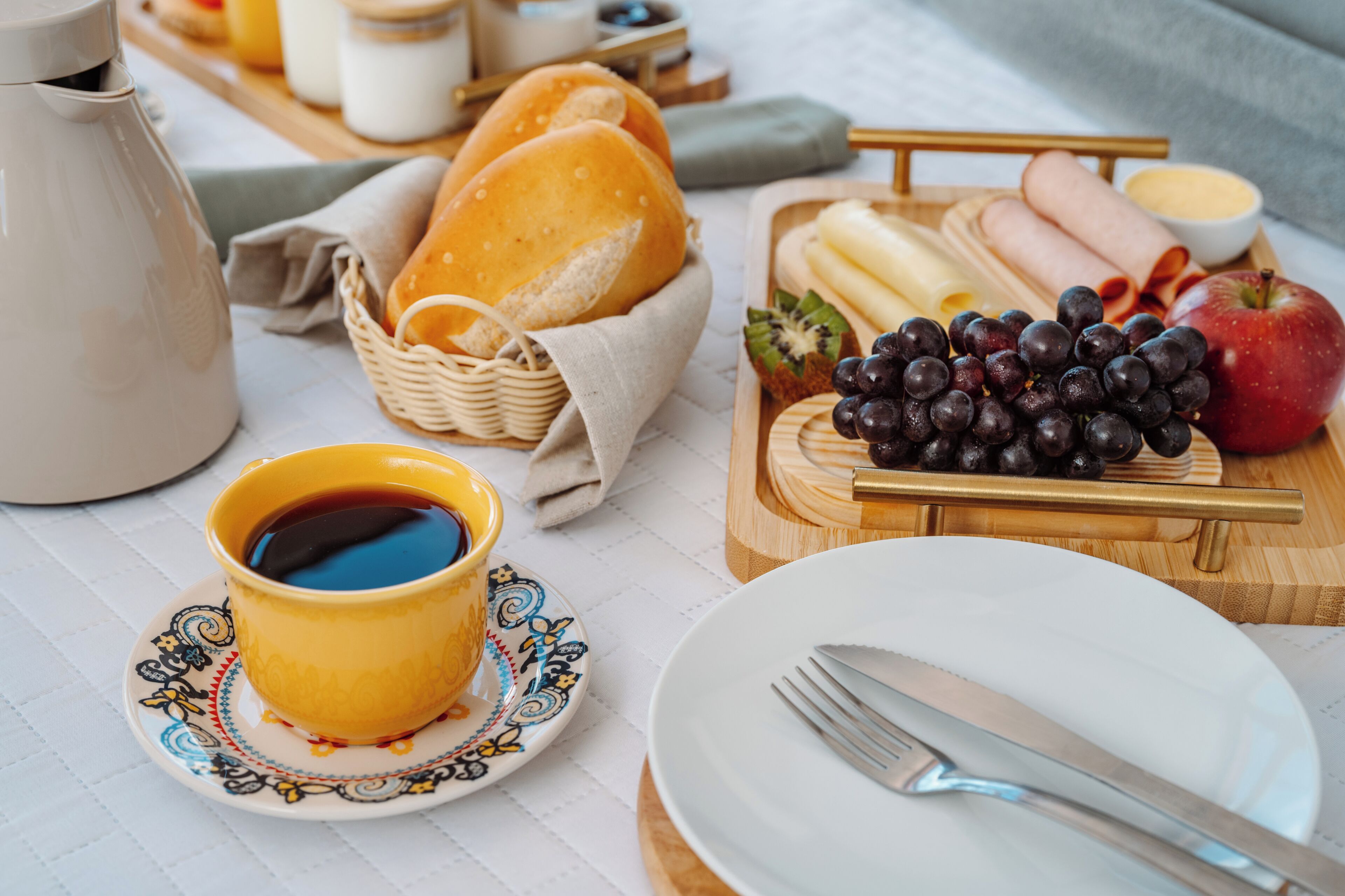 A breakfast setting with bread, fruits, cheese, and a cup of coffee.