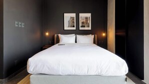 Une chambre d’hôtel moderne avec un grand lit, deux lampes fixées au mur et deux tableaux encadrés accrochés au mur.