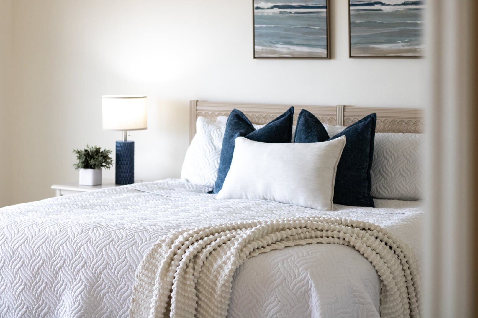 A neatly made bed with a white quilt and a decorative white throw blanket.