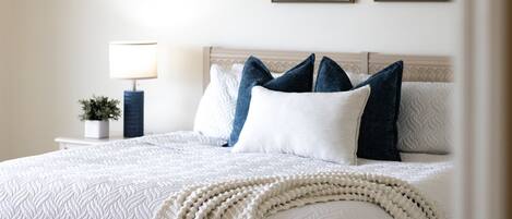 A neatly made bed with a white quilt and a decorative white throw blanket.