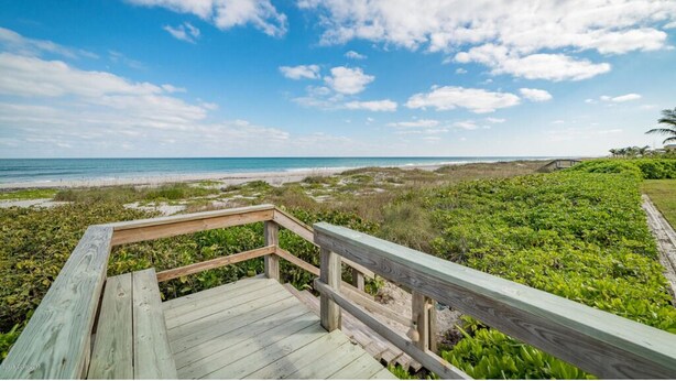 A wooden deck leading to a beach with a clear sky and distant ocean view. - Gorgeous Oceanfront Condo With Double Wide Balcony & Complex Pool 🏝️🍹 (Cocoa Beach)