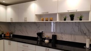 Cozinha moderna com armários brancos, bancada preta e painel de mármore.