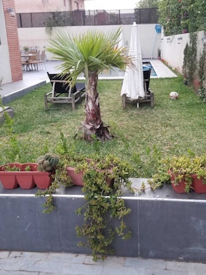 A small outdoor area with a palm tree, a white umbrella, and a bench. - Pleasant family stay in a superb 5-bedroom villa with private pool. (Marrakech)