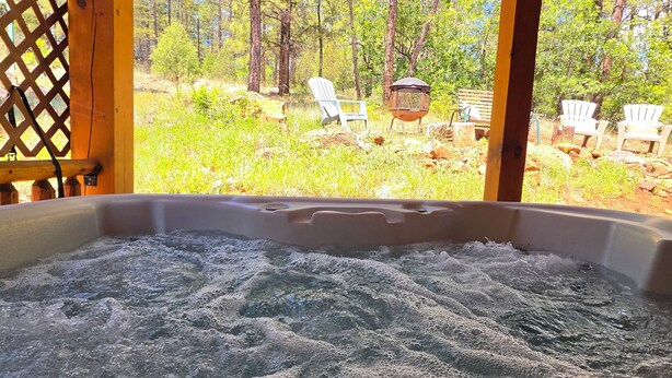 A hot tub with a view of a forested area and outdoor seating. - Cozy Log Cabin Retreat :: Hot Tub :: Forest Views (Flagstaff)