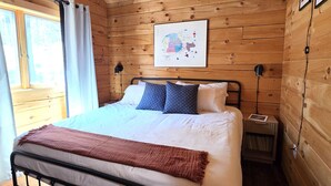 A wooden cabin bedroom with a bed, ceiling fan, map on the wall, and a nightstand. - Cozy Log Cabin Retreat :: Hot Tub :: Forest Views (Flagstaff)